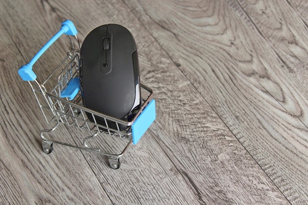 Computer mouse inside shopping trolley on wooden table with copy space Online shopping concept