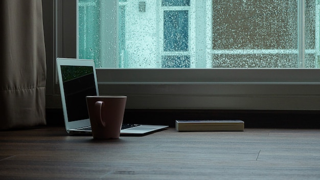 Computer notebook next to a cup coffee on rainy day window background 