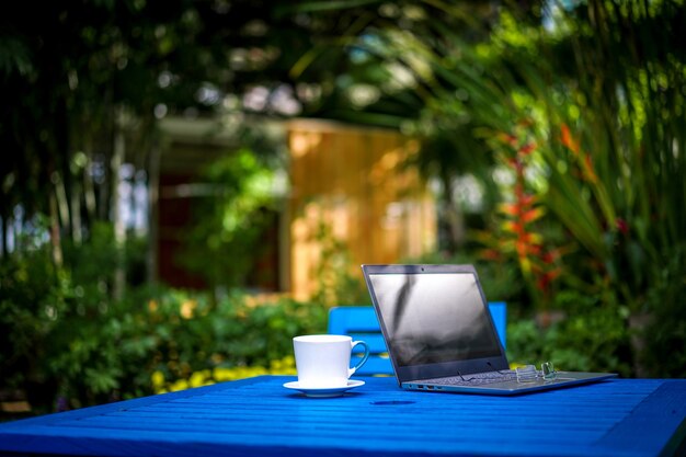 Computer Notebook / Laptop, glasses with the white coffee cup on the dark blue table in the afternoon relaxation time.