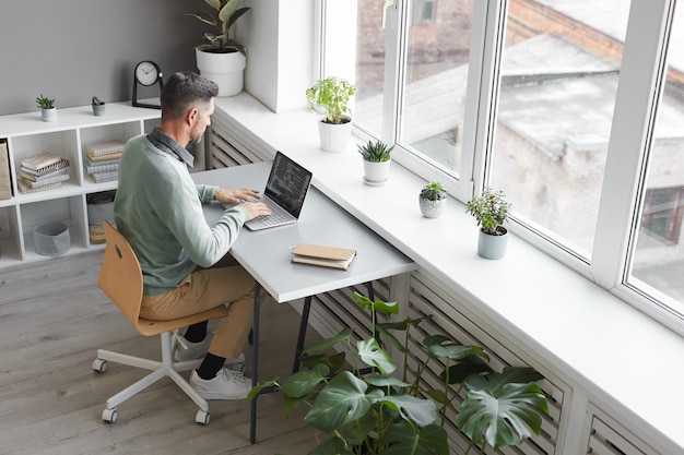 Computer programmer sitting at his workplace typing on laptop in spacious office