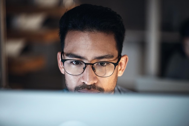 Computer research and man in glasses for software development night programming and cybersecurity Reading focus and person or programmer with data analysis desktop system and coding information