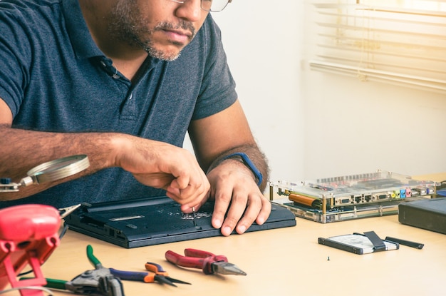 Computer Technician Fixing Laptop On Desk. Black man. Work tools.