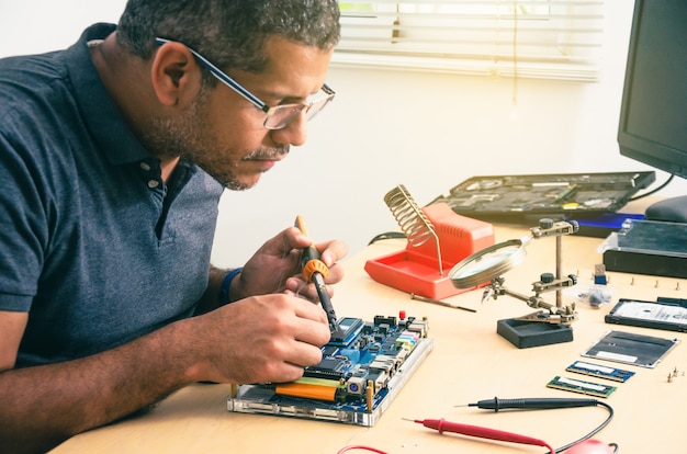 Computer Technician Wearing Glasses, Fixing Laptop On Desk, With Tools Around. Black man. Work tools.