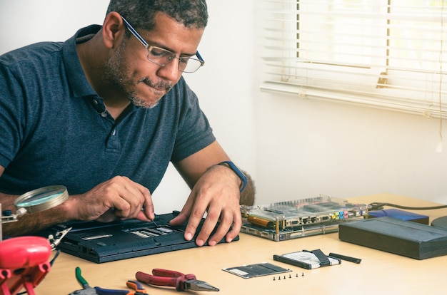 Computer Technician Wearing Glasses, Fixing Laptop On Desk, With Tools Around. Black man. Work tools.