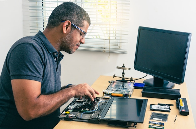 Computer Technician Wearing Glasses, Fixing Laptop On Desk, With Tools Around. Black man. Work tools.