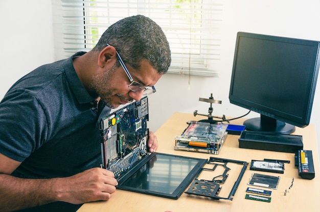 Computer Technician Wearing Glasses, Fixing Laptop On Desk, With Tools Around. Black man. Work tools.