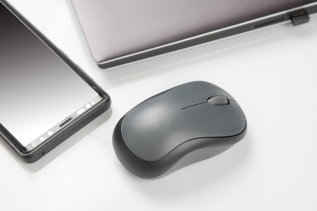 Computer wireless mouse next to a laptop on a white table closeup electronic personal industry