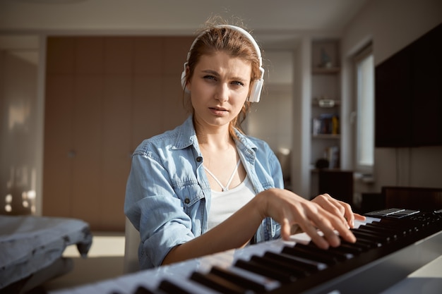 Concentrate female person wearing headphones while plying the synthesizer, being at home