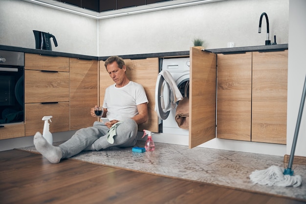 Concentrated adult man staring at his smartphone while reading message during drinking coffee at home