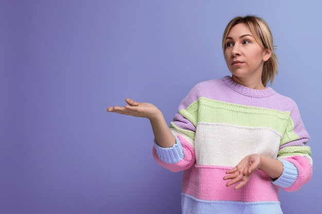 Concentrated blond young woman demonstrates free space on purple background with copy space