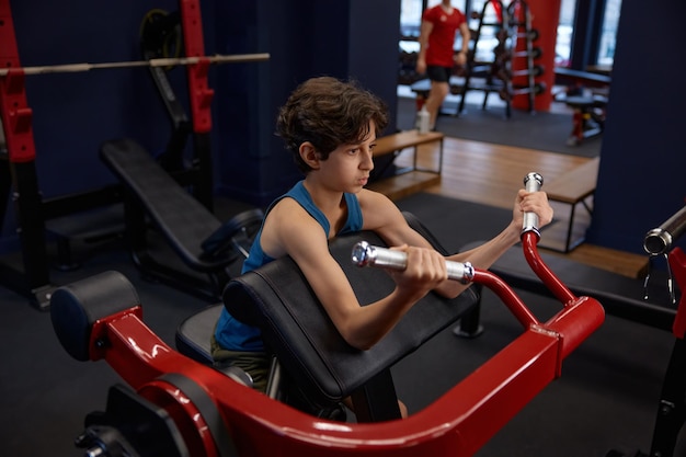 Concentrated boy doing sports exercise for strong arms while training in gym