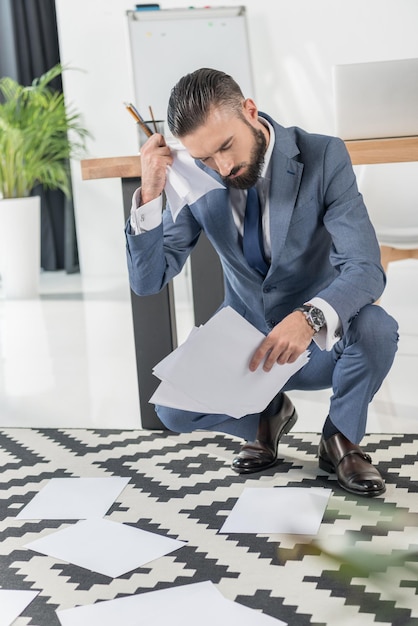 Concentrated businessman looking at papers on floor at modern office