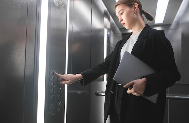 Concentrated businesswoman pressing the button of the elevator holding laptop in her hand.