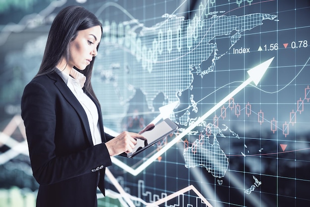 Concentrated businesswoman using digital tablet on virtual wall background with stock market changes numbers forex dynamics map and glowing raising arrows World trade market concept