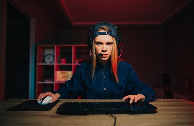 Concentrated cute female gamer in cap and headset playing online games at home on computer