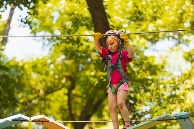 The concentrated girl carefully overcomes obstacles in the rope park