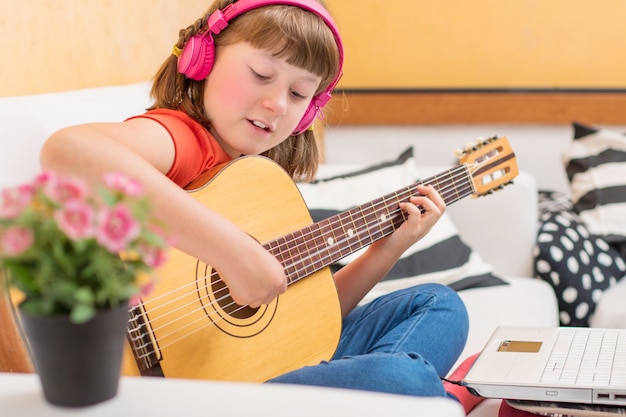 Concentrated girl is practicing with acoustic guitar sit on sofa at home