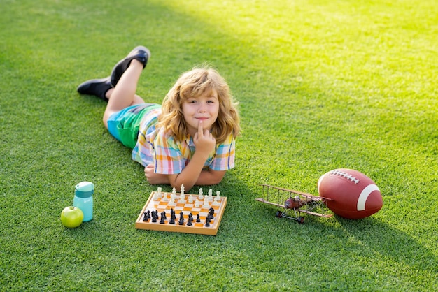 Concentrated kid developing chess strategy playing board game in backyard laying on grass