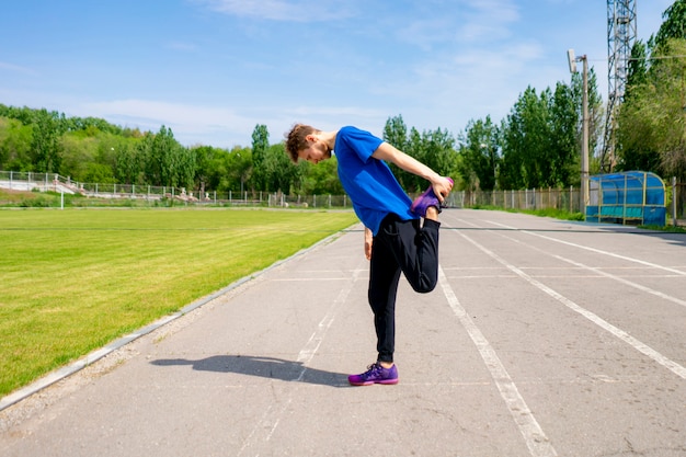 Concentrated male athlete outdoor stretching his body in sportswear doing healthy practises