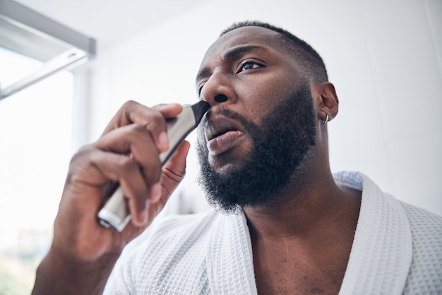 Concentrated male person being in the bathroom while taking care of his appearance