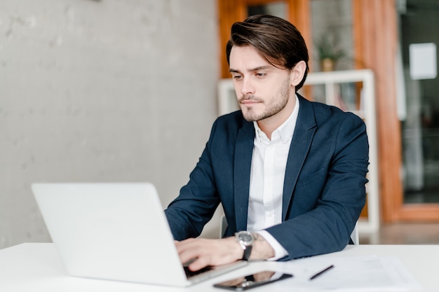 Concentrated man in suit typing on laptop in the office