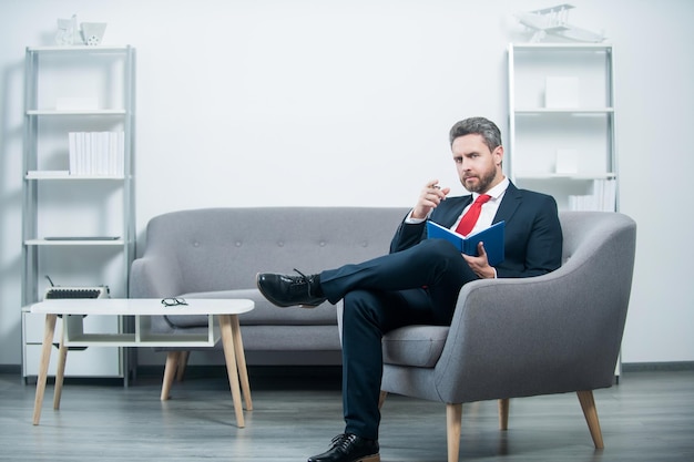 Concentrated mature businessman in suit sit in office reading book