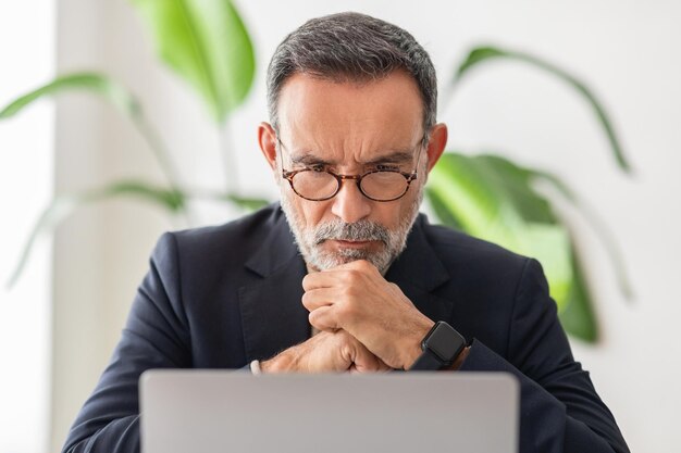 Concentrated mature businessman with glasses deep in thought resting chin on hands