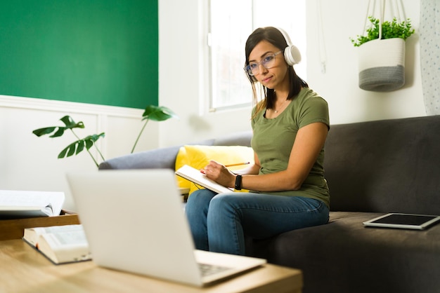 Concentrated mid- adult university student taking notes and listening to her online teacher during a virtual class