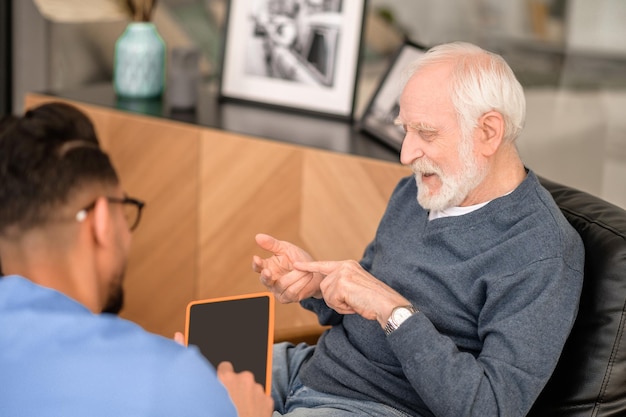 Concentrated pensioner enumerating something in conversation with his caregiver