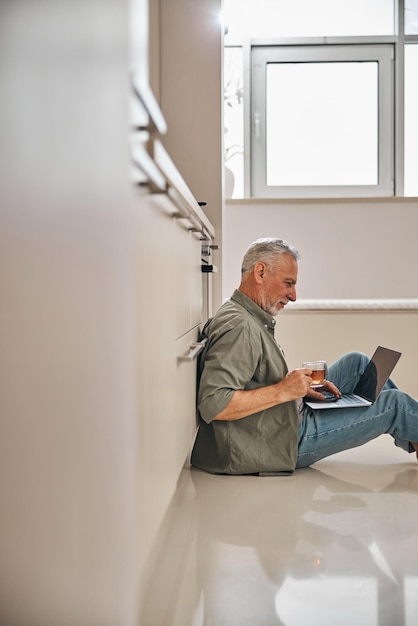 Concentrated senior gentleman working on laptop and sitting on floor