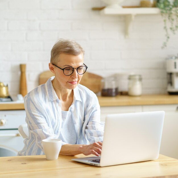 Concentrated senior woman writer typing something on laptop while working online from home