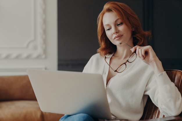 Concentrated serious redhead woman makes remote job indoors