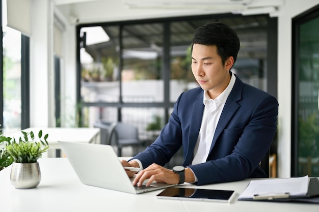 Concentrated and smart Asian businessman using laptop at his desk