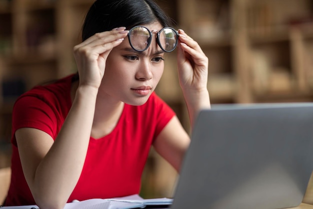 Concentrated smart teen korean female student takes off glasses watch online lesson in laptop