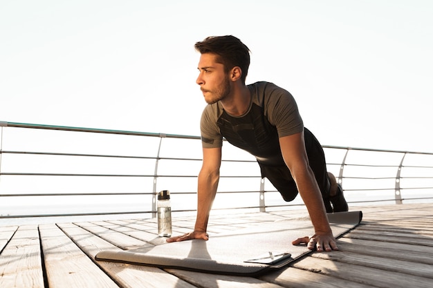 Concentrated sports man outdoors on the beach makes sport exercises