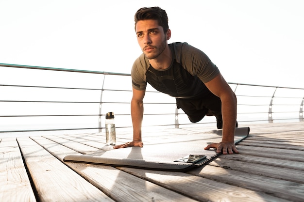 Concentrated sports man outdoors on the beach makes sport exercises