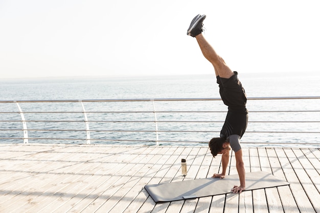 Concentrated sports man outdoors on the beach makes sport exercises