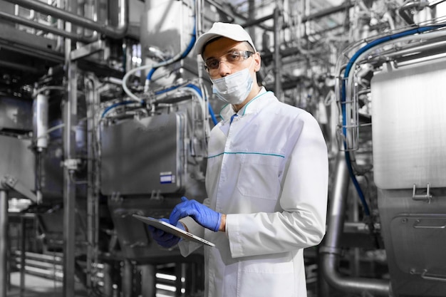 Concentrated technologist taking necessary notes with help of digital tablet while standing at production department of dairy factory inspector carries out control at the cheese factory