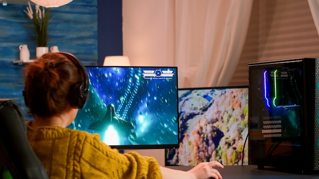 Concentrated woman gamer sitting on desk, wearing headset starts playing space shooter video game