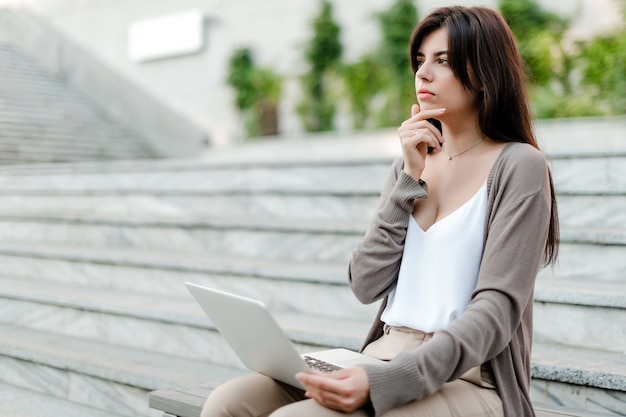 Concentrated woman thinking sitting with laptop outdoors