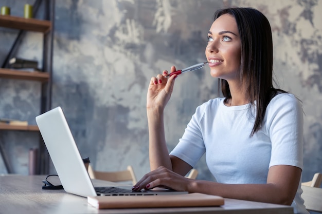 Concentrated at work. Confident young woman in smart casual wear working on laptop while sitting near window in creative office or cafe.