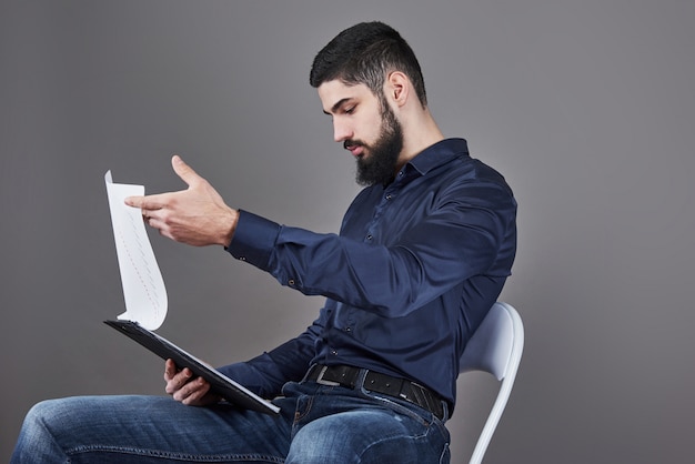 Concentrated young attractive businessman in blue shirt planning and writing in clipboard