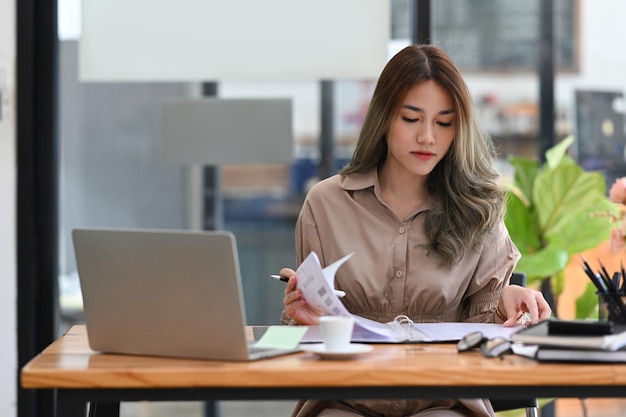 Concentrated young businesswoman checking financial reports and using computer laptop