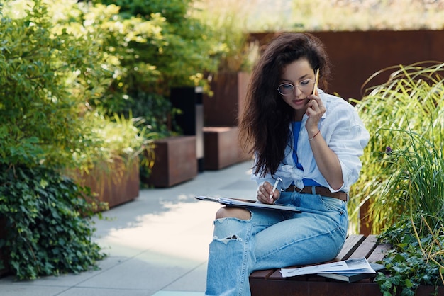 Concentrated young female entrepreneur in casual clothes and glasses examining documents while