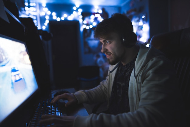 A concentrated young man plays on a computer in a cozy room.