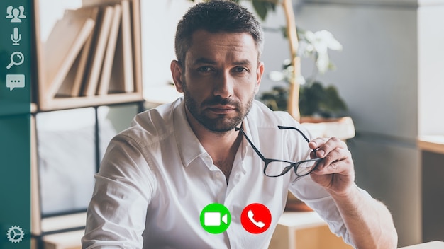 Concentrated young man in shirt looking at camera while having video call