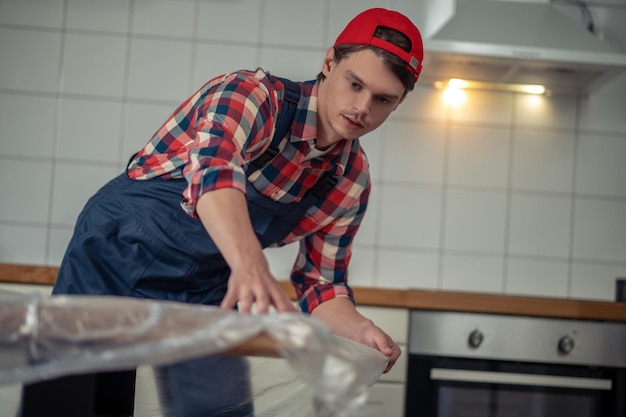 Concentrated young serviceman wrapping the wooden tabletop