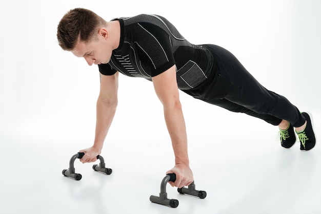 Concentrated young sportsman doing push ups with gym equipment