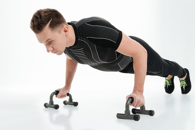 Concentrated young sportsman doing push ups with gym equipment