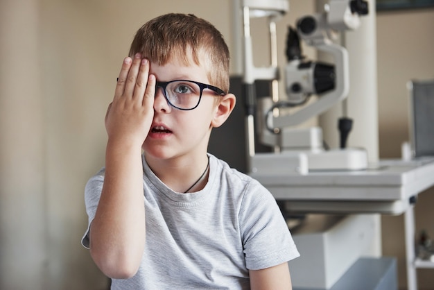 Concentrating on images. Little boy covering his eye and have reviewing eyesight in the clinic.